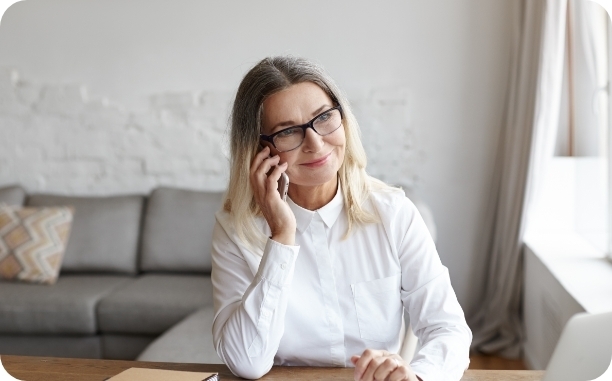 a smiling woman sitting at a table with a cellphone to her ear